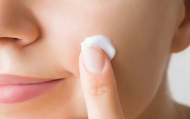 Creme unter einem Finger im Gesicht einer Frau