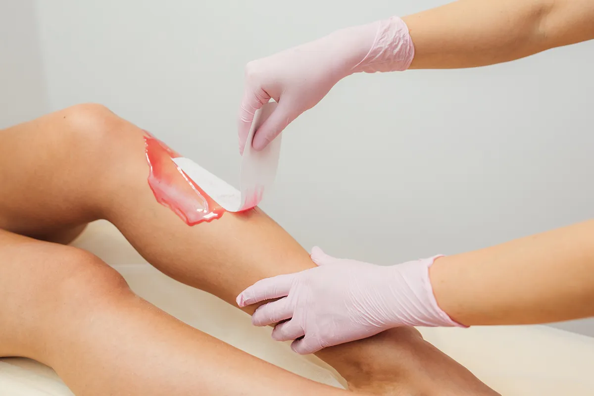 Auf einem Bein wird durch eine andere Person eine rote Creme aufgetragen