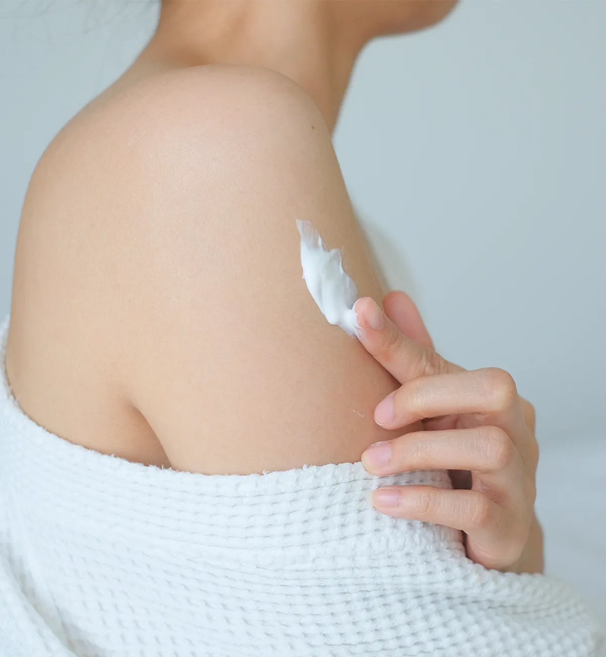 Seitenansicht einer weibliche Person, die Creme auf ihrem rechten Oberarm verreibt