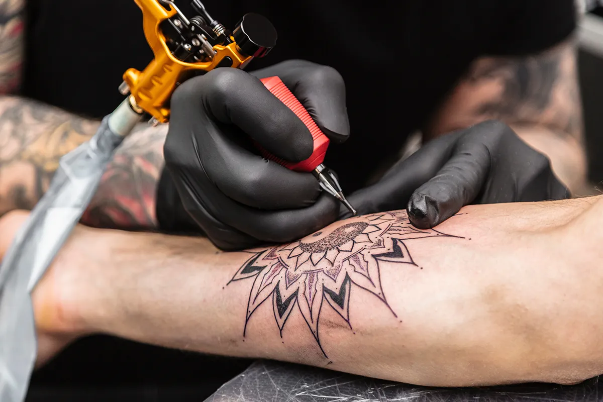 Koerperliche Voraussetzungen Schmerzempfinden bei Tätowierungen Nahaufnahme eines Unterarms der tätowiert wird