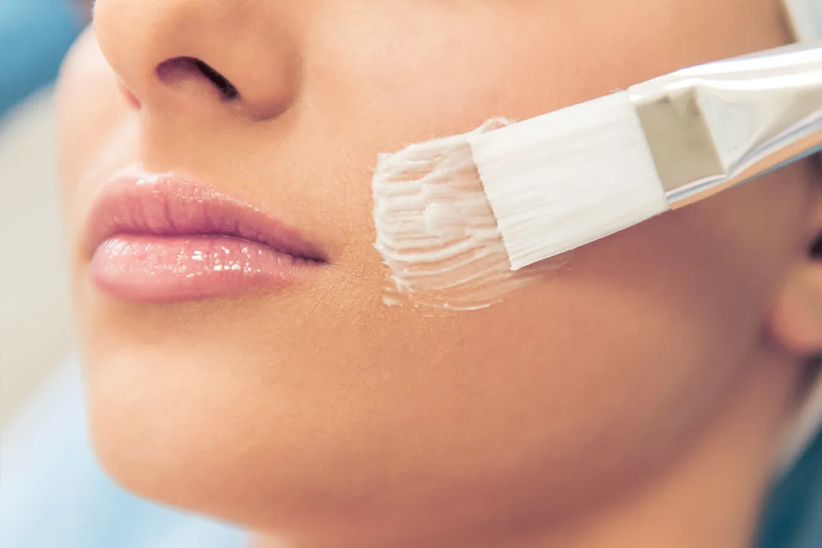 Creme wir mit einem Pinsel im Gesicht einer weiblichen Person verstrichen