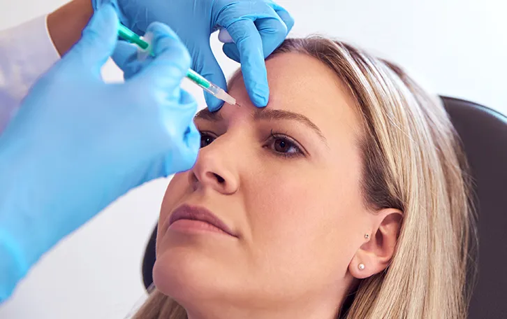 Ein medizinisches Personal setzt eine Spritze auf der Stirn einer sitzenden Person an