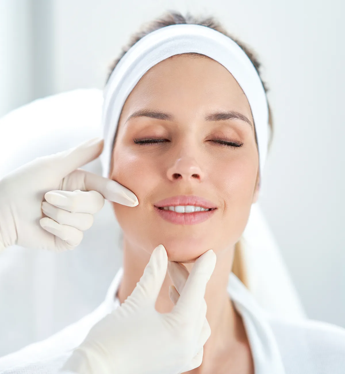 Eine weibliche Person mit geschlossenen Augen wird von zwei Händen in Latex-Handhschuhen im Gesicht gegriffen