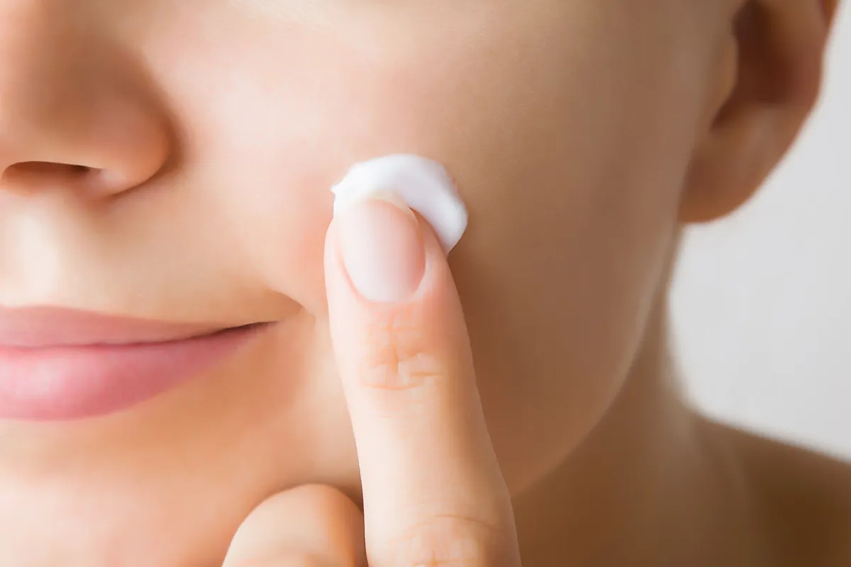 Creme unter einem Finger im Gesicht einer weiblichen Person